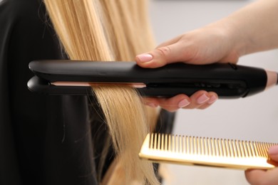 Photo of Hairdresser straightening woman's hair in salon, closeup