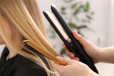 Photo of Hairdresser straightening woman's hair in salon, closeup