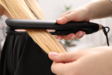 Photo of Hairdresser straightening woman's hair in salon, closeup
