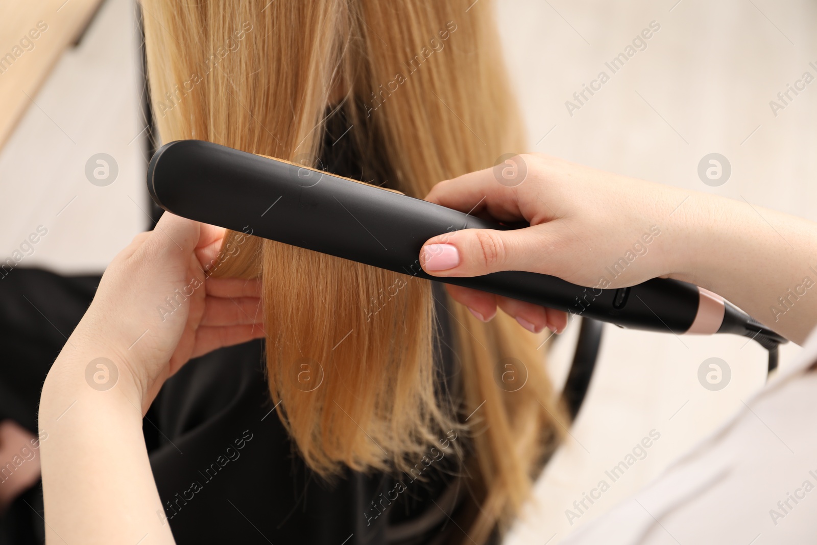 Hairdresser straightening woman's hair in salon, closeup Photo of Hairdresser straightening woman's hair in salon, closeup