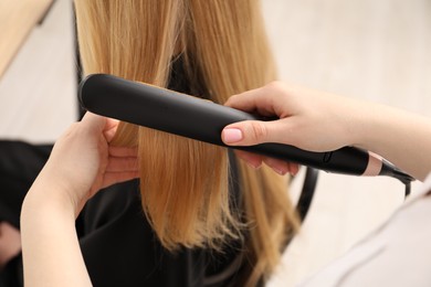 Photo of Hairdresser straightening woman's hair in salon, closeup