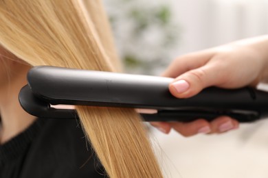 Photo of Hairdresser straightening woman's hair in salon, closeup