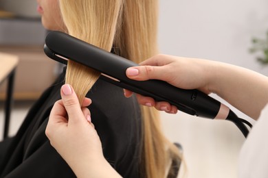 Photo of Hairdresser straightening woman's hair in salon, closeup