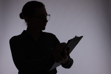 Photo of Silhouette of woman with clipboard on grey background, space for text