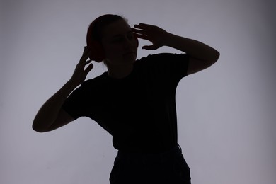 Photo of Silhouette of woman in headphones listening to music on grey background