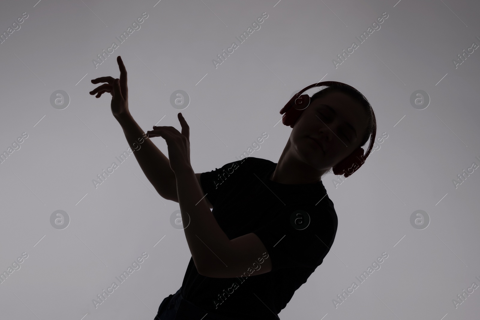 Silhouette of woman in headphones listening to music on grey background Photo of Silhouette of woman in headphones listening to music on grey background