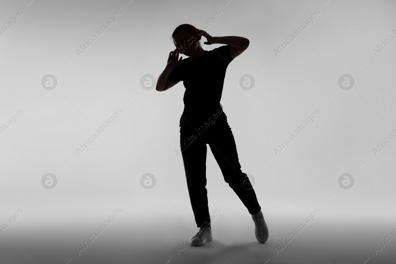 Silhouette of woman in headphones listening to music on grey background Photo of Silhouette of woman in headphones listening to music on grey background