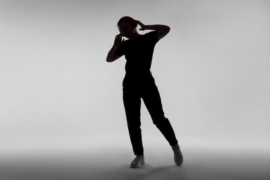 Photo of Silhouette of woman in headphones listening to music on grey background