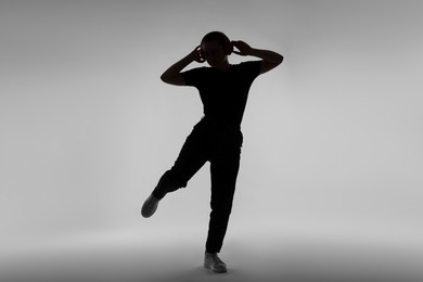 Photo of Silhouette of woman in headphones listening to music on grey background