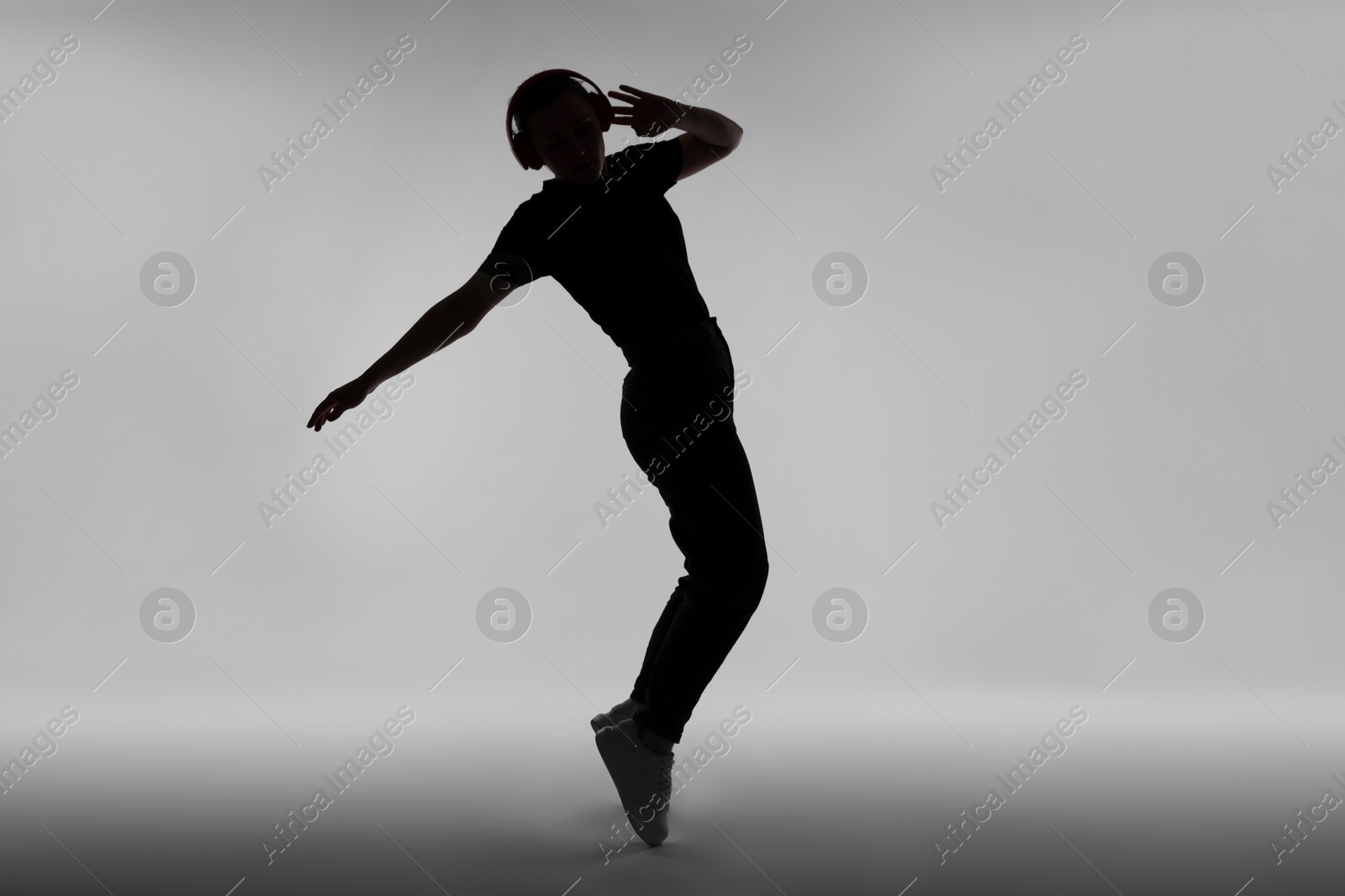 Silhouette of man in headphones listening to music on grey background Photo of Silhouette of man in headphones listening to music on grey background