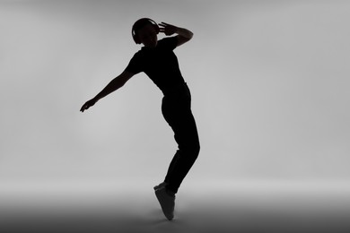 Photo of Silhouette of man in headphones listening to music on grey background