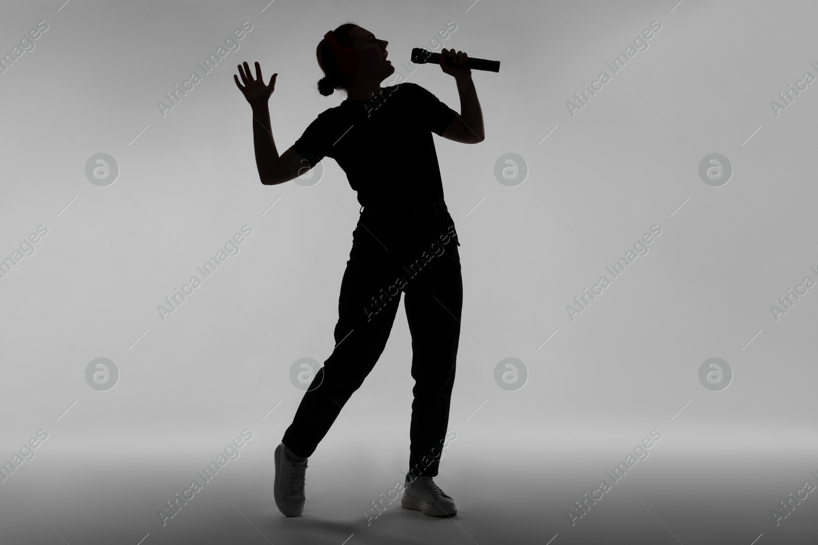 Silhouette of woman singing on grey background Photo of Silhouette of woman singing on grey background