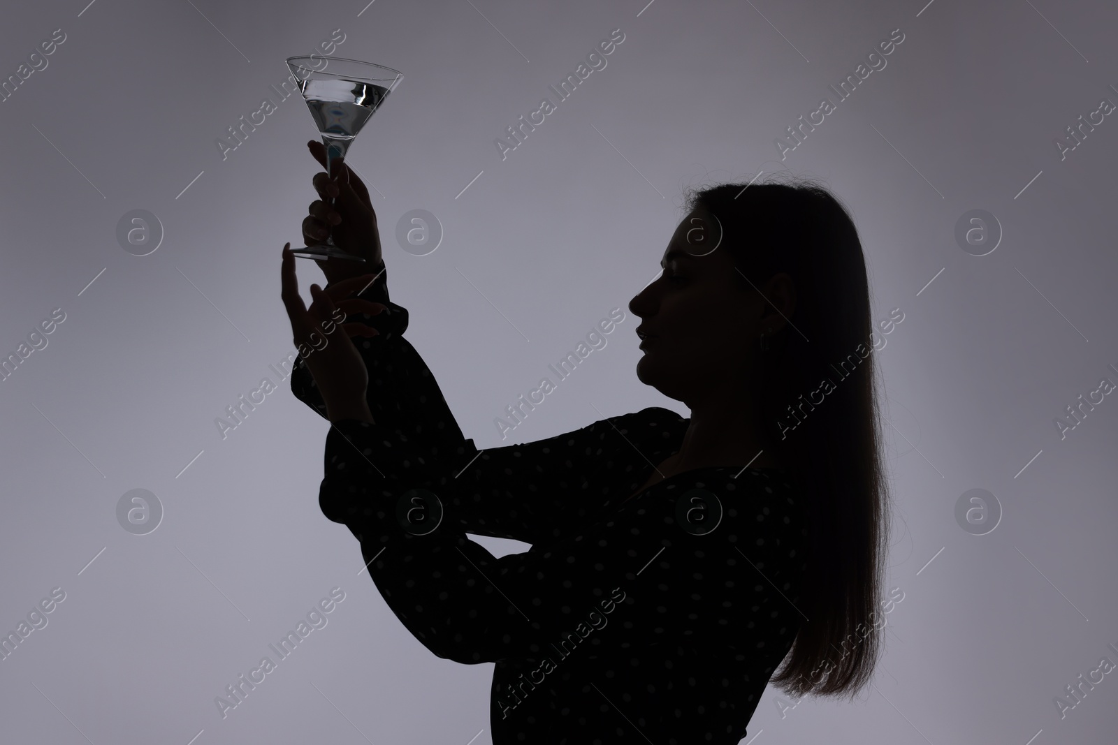 Silhouette of woman with glass of drink on grey background Photo of Silhouette of woman with glass of drink on grey background