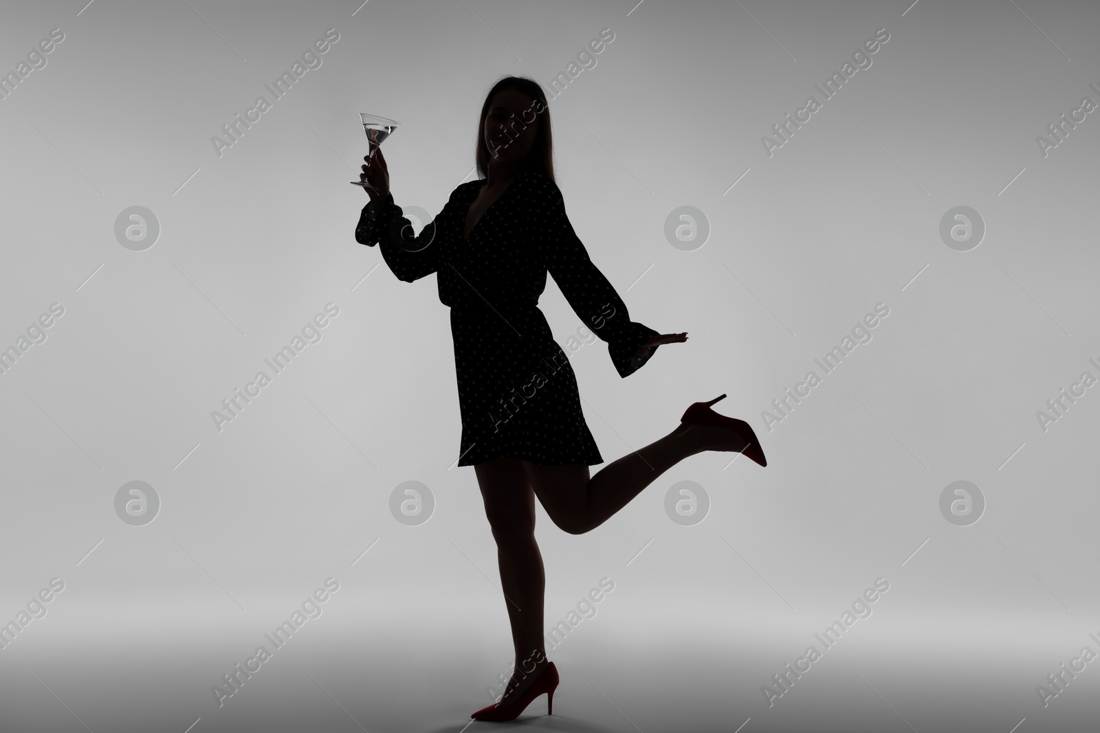 Silhouette of woman with glass of drink on grey background Photo of Silhouette of woman with glass of drink on grey background