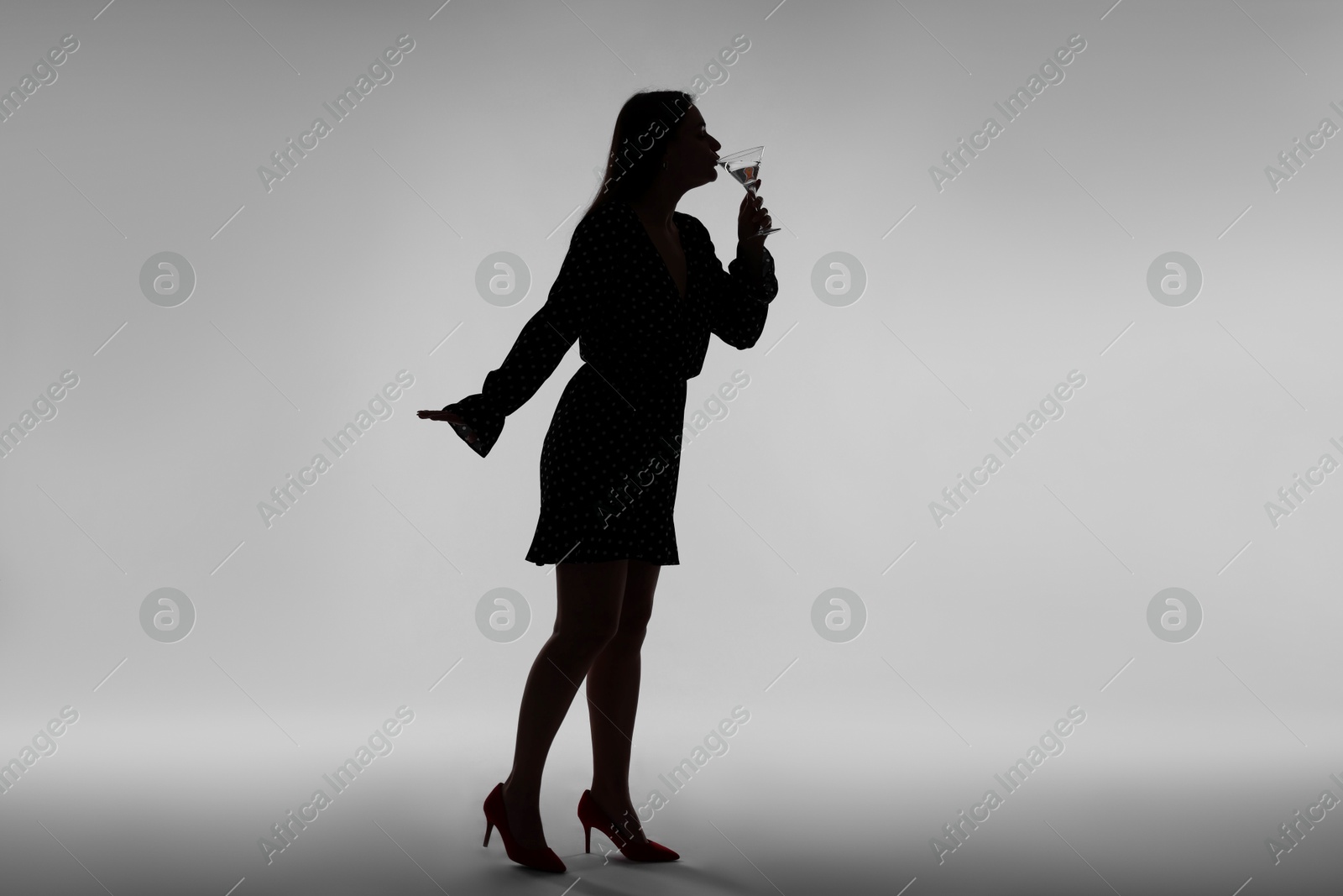 Silhouette of woman with glass of drink on grey background Photo of Silhouette of woman with glass of drink on grey background