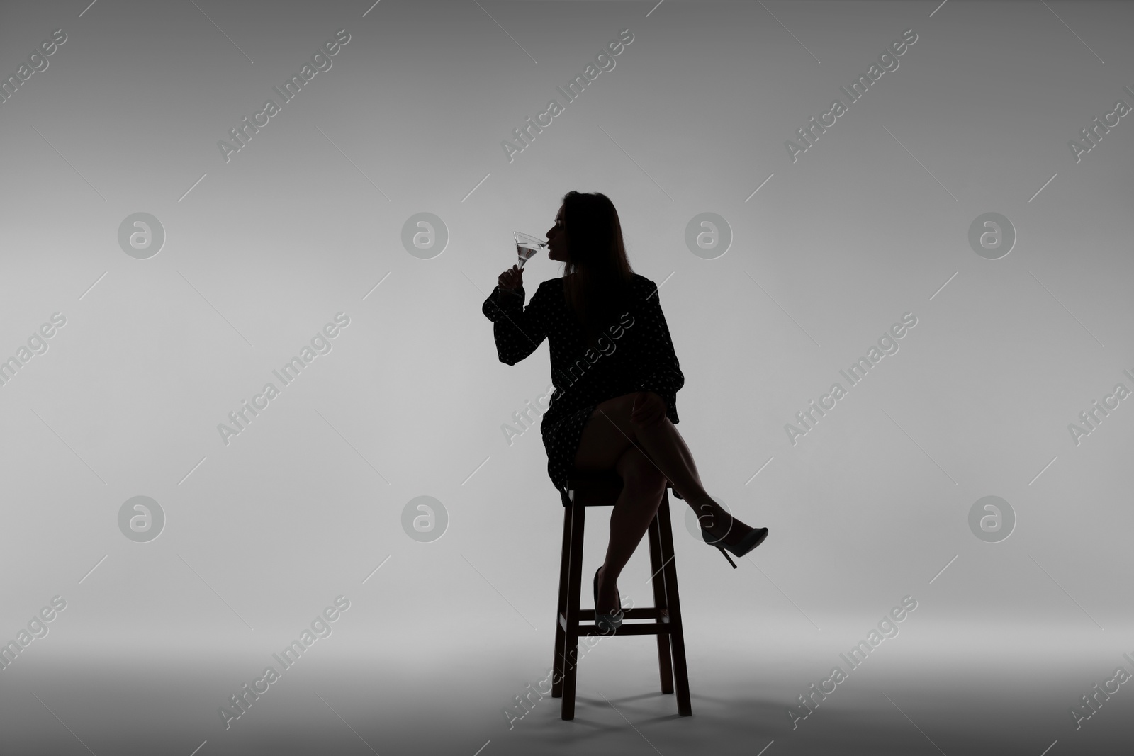 Silhouette of woman with glass of drink on grey background Photo of Silhouette of woman with glass of drink on grey background