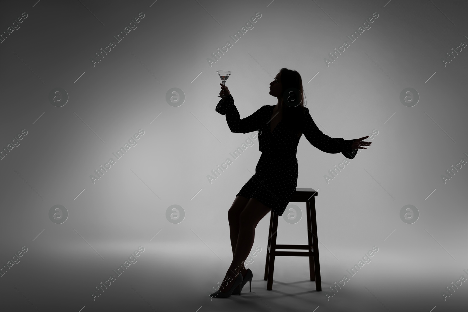 Silhouette of woman with glass of drink on grey background Photo of Silhouette of woman with glass of drink on grey background