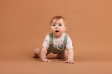 Photo of Cute little baby crawling on pale brown background
