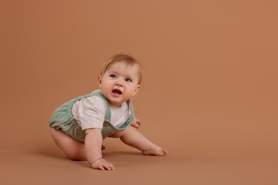 Photo of Cute little baby crawling on pale brown background, space for text