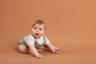 Photo of Cute little baby crawling on pale brown background, space for text