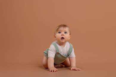 Photo of Cute little baby crawling on pale brown background