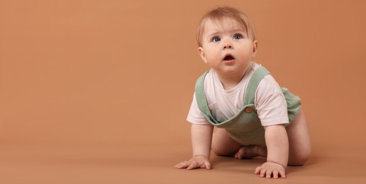 Photo of Cute little baby crawling on pale brown background, space for text