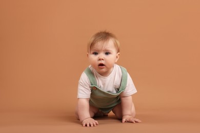 Photo of Cute little baby crawling on pale brown background