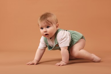 Photo of Cute little baby crawling on pale brown background