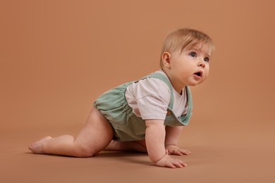 Photo of Cute little baby crawling on pale brown background