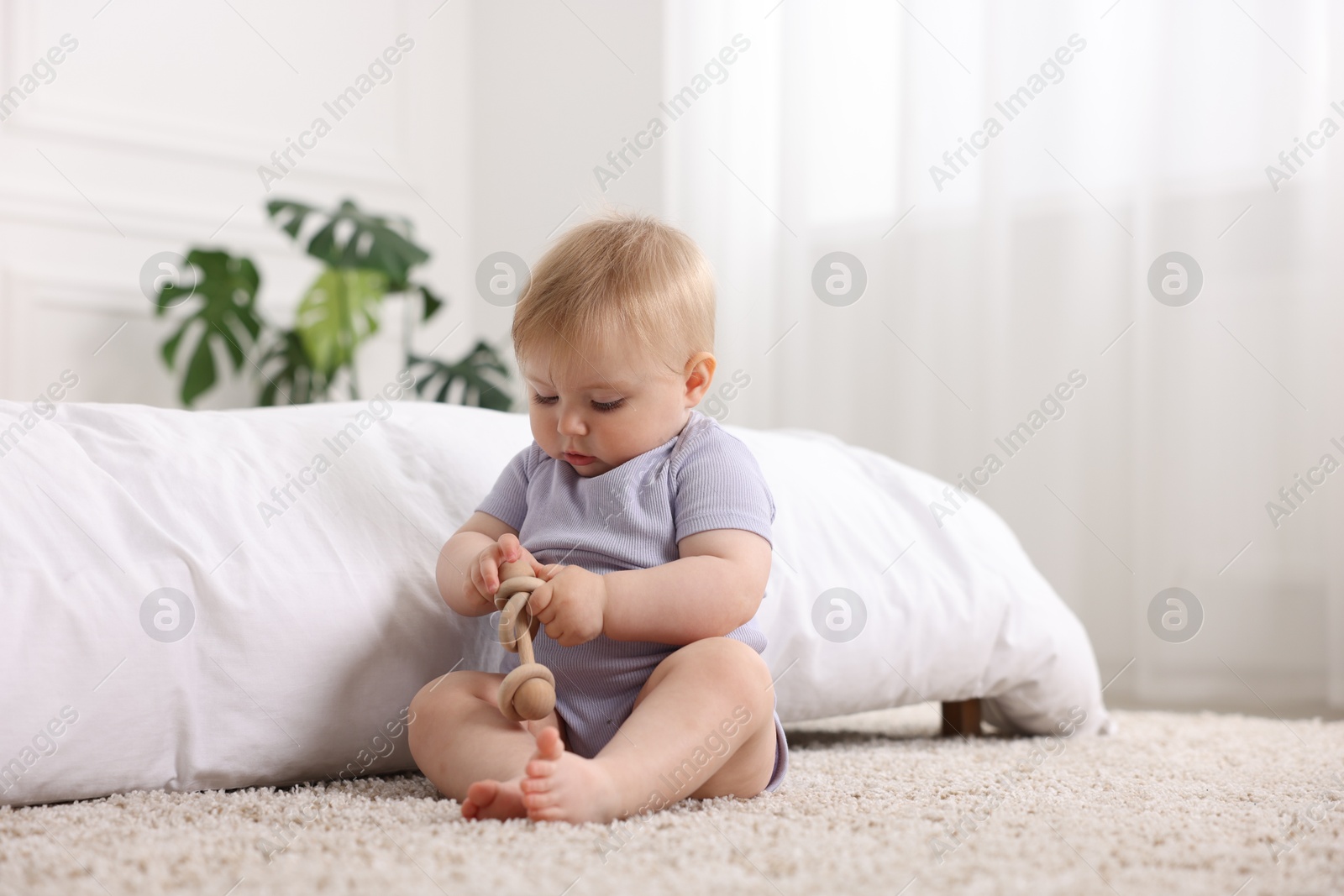 Photo of Cute little baby playing with rattle on floor indoors