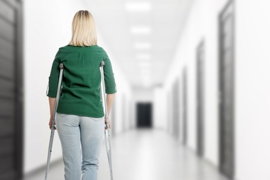 Image of Woman with axillary crutches in hospital, back view. Space for text