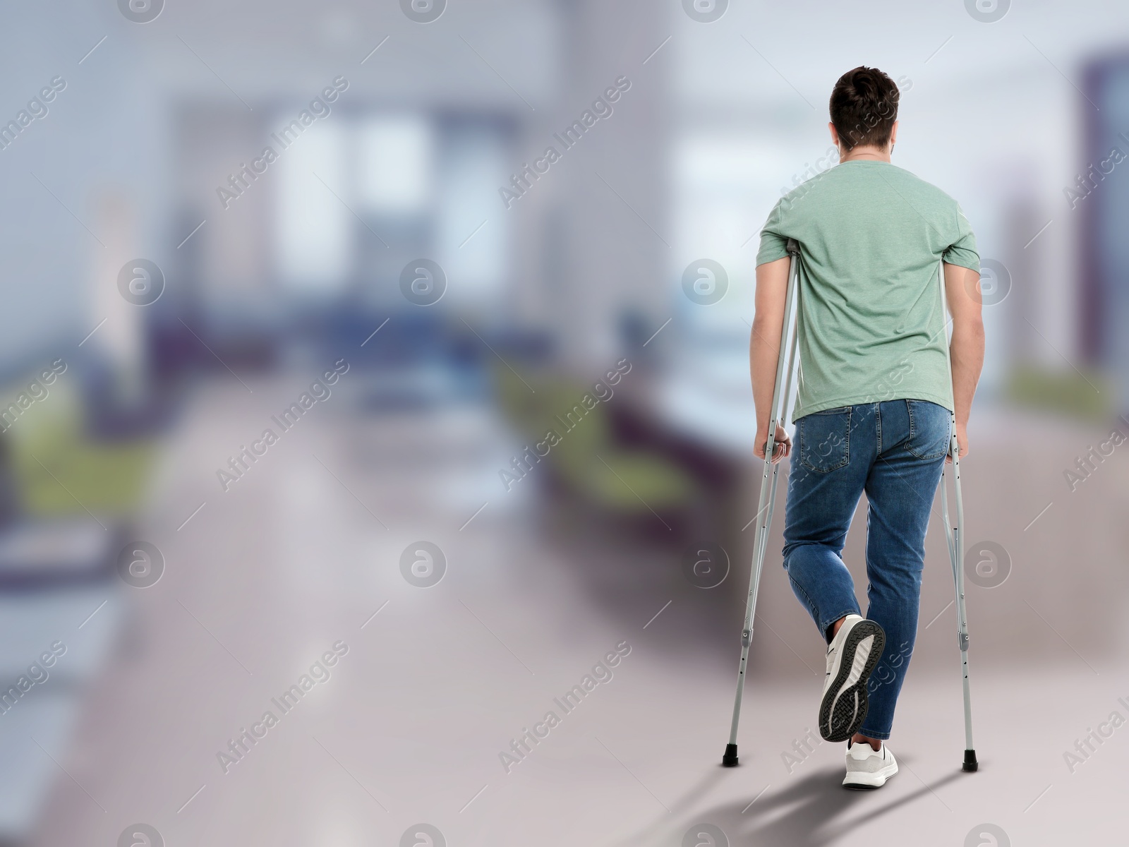 Man with axillary crutches in hospital, back view. Space for text Image of Man with axillary crutches in hospital, back view. Space for text