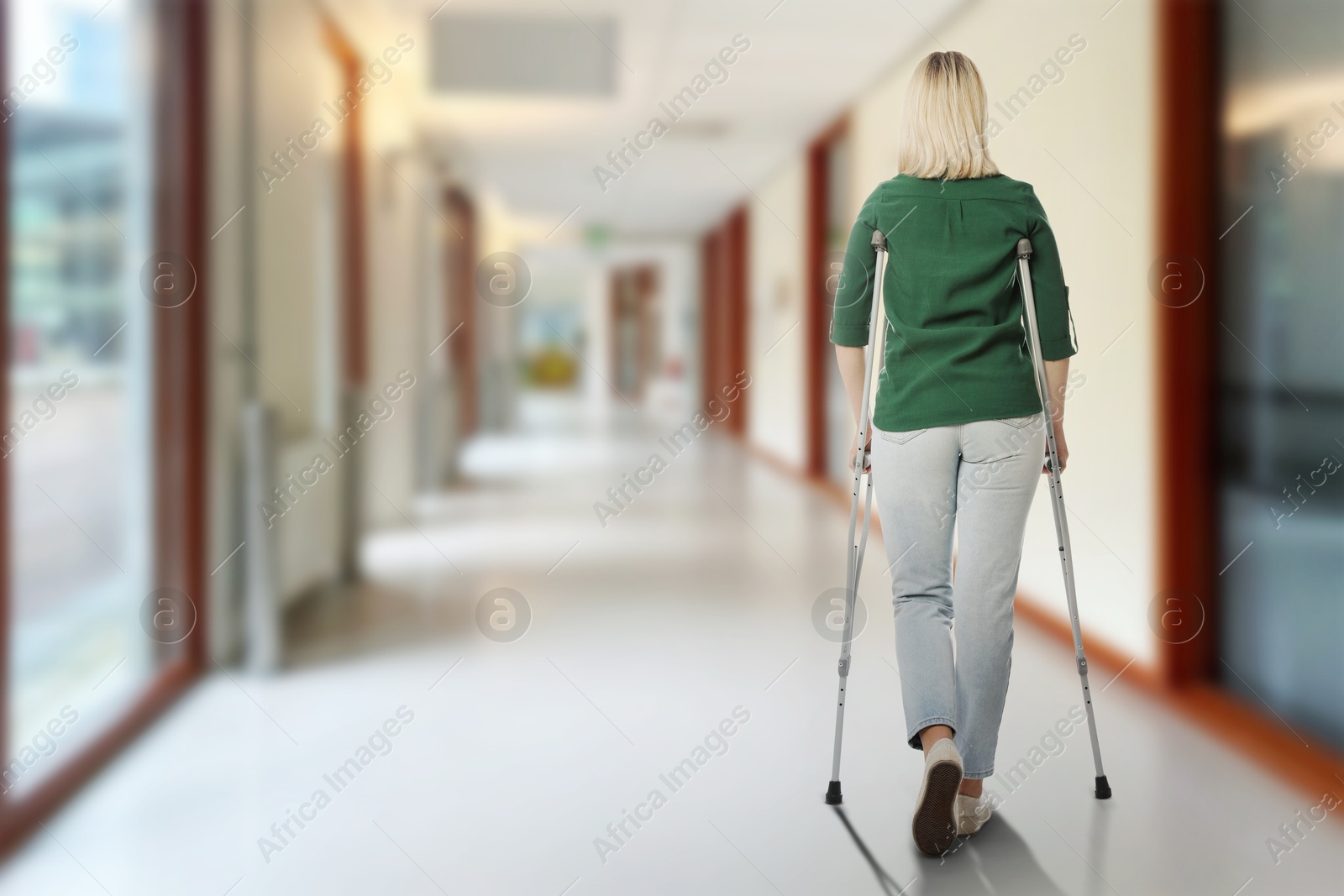Woman with axillary crutches in hospital, back view. Space for text Image of Woman with axillary crutches in hospital, back view. Space for text