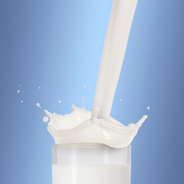 Image of Pouring fresh milk into glass against light blue background. Liquid splashing out of glass