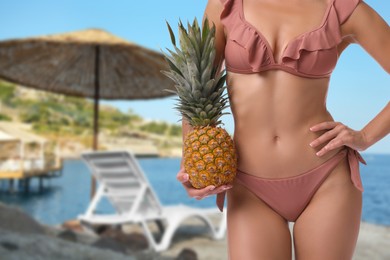 Image of Pretty woman in swimsuit holding pineapple on beautiful tropical beach, closeup