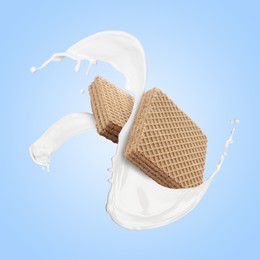 Image of Tasty crispy wafers and splashing milk on light blue background