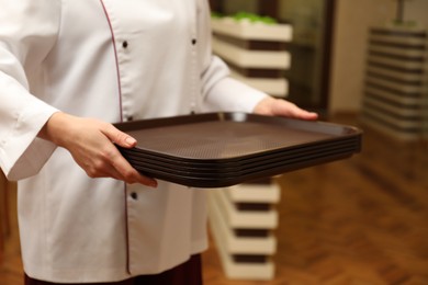 Photo of School canteen worker holding plastic trays for food indoors, closeup