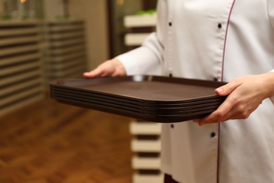 Photo of School canteen worker holding plastic trays for food indoors, closeup