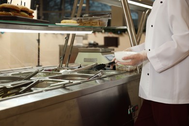 Photo of School canteen worker at serving line, closeup. Tasty food