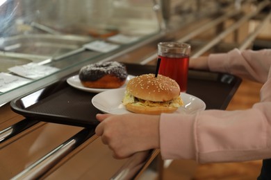 Photo of Little girl with plastic tray near serving line in canteen, closeup. School food
