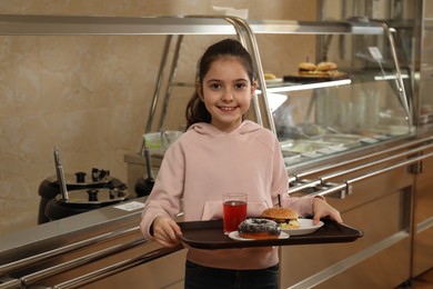 Photo of Little girl with plastic tray near serving line in canteen. School food
