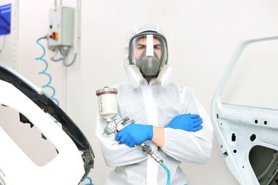 Photo of Worker with spray painting gun and car in body shop