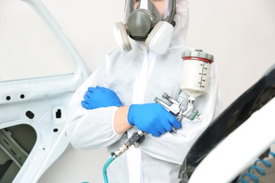 Photo of Worker with spray painting gun and car in body shop, closeup
