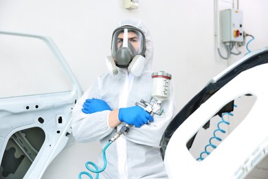 Photo of Worker with spray painting gun and car in body shop
