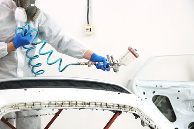 Photo of Worker painting car in body shop, closeup
