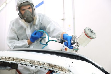 Photo of Worker painting car in body shop, selective focus