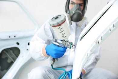 Photo of Worker painting car in body shop, selective focus
