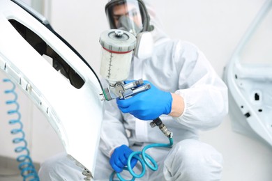 Photo of Worker painting car in body shop, selective focus
