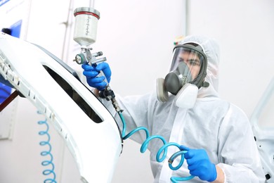 Photo of Worker spray painting car in body shop