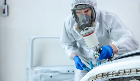 Photo of Worker spray painting car in body shop. Space for text